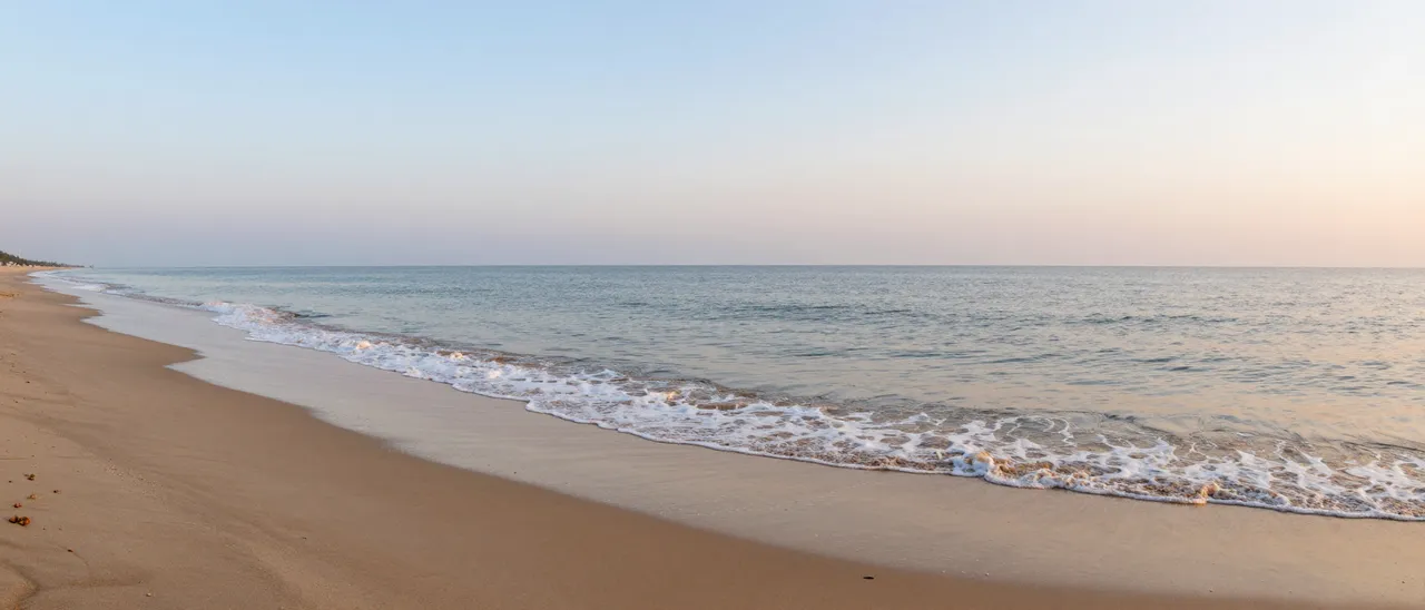 Gentle foamy ocean waves lap a quiet sandy shore under a soft gradient pastel sky