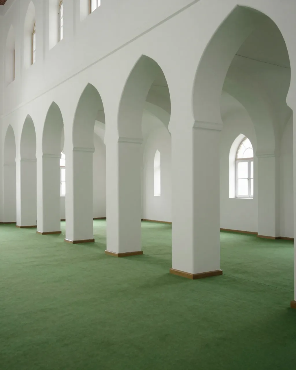 Empty prayer hall with rows of white pointed arches over a soft plain green carpet