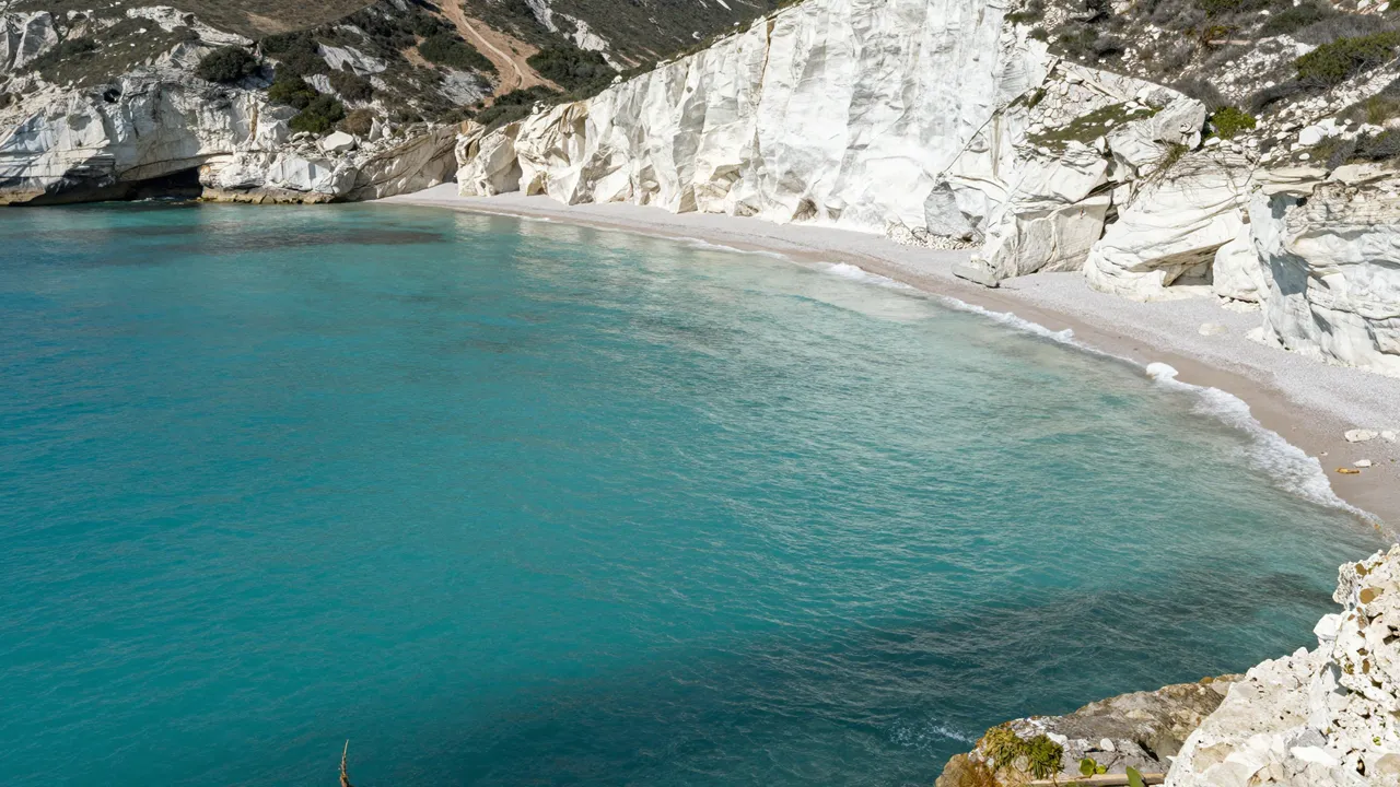 A quiet sheltered cove with bright turquoise water bordered by steep white chalk cliffs and a pale sandy beach