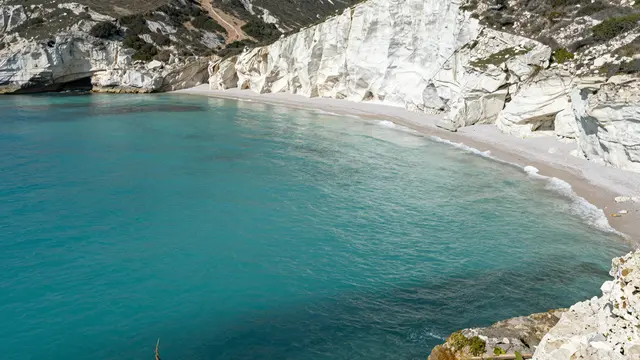 A quiet sheltered cove with bright turquoise water bordered by steep white chalk cliffs and a pale sandy beach
