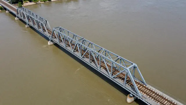 Aerial view of a steel truss railway bridge carrying track across a wide murky brown river
