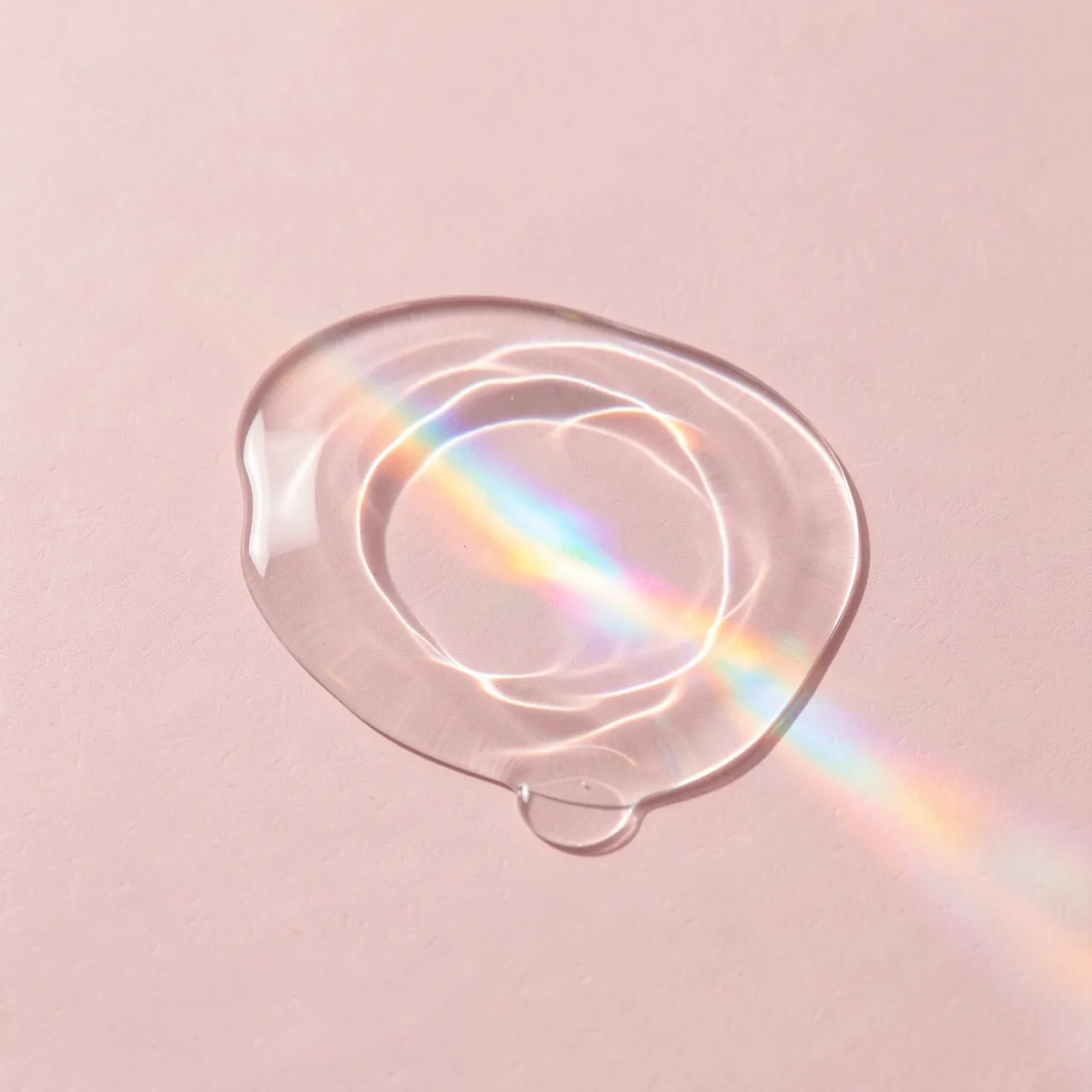 Translucent rippled fluid pool casts iridescent rainbow caustics onto a pale pink background