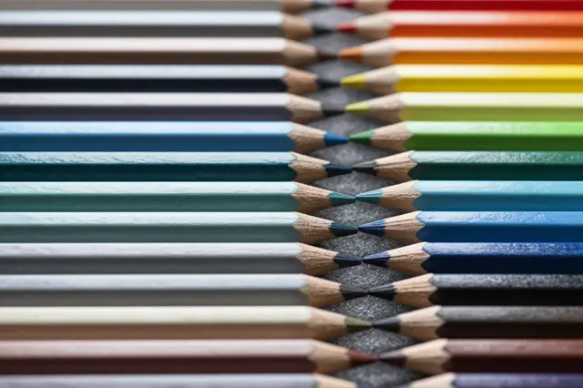 Top view of sharpened colored pencils arranged in a symmetric rainbow pattern on a dark textured surface