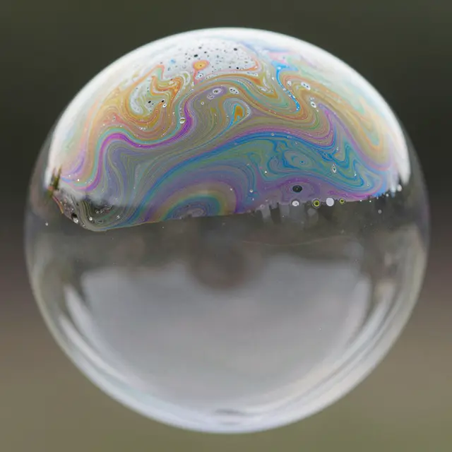 Close-up macro of a soap bubble with swirling iridescent rainbow patterns across its upper surface
