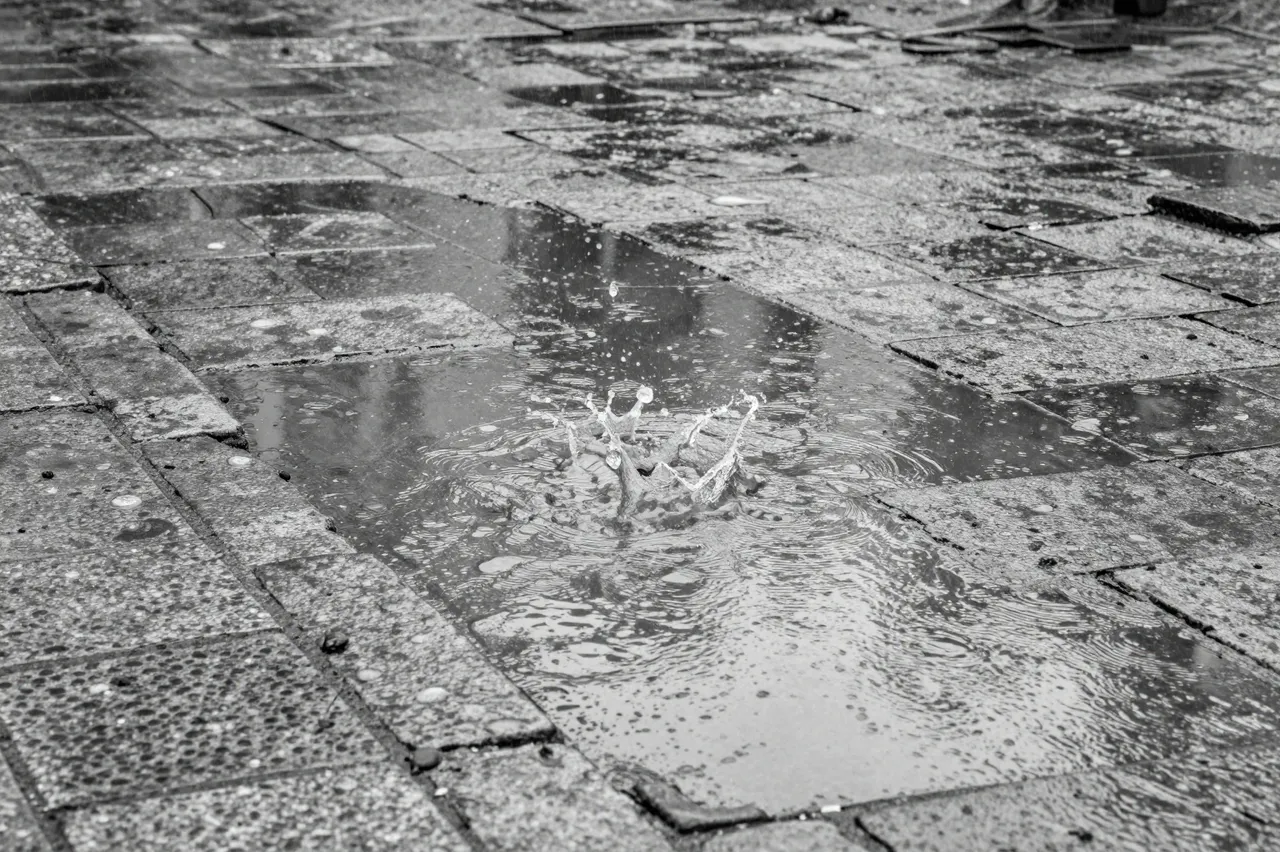 A raindrop creates a crown-shaped splash in a puddle on weathered old paving stones