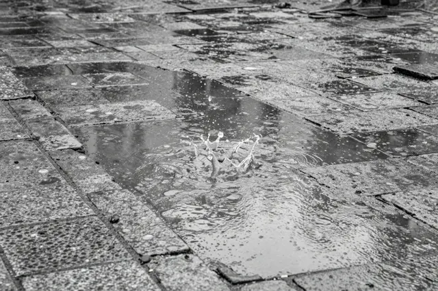 A raindrop creates a crown-shaped splash in a puddle on weathered old paving stones