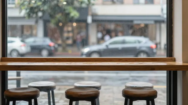 Wooden cafe window counter with stools overlooking a softly blurred rainy street