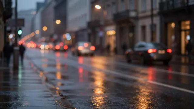 Out of focus rainy evening city street with glowing red and amber bokeh light reflections on wet pavement
