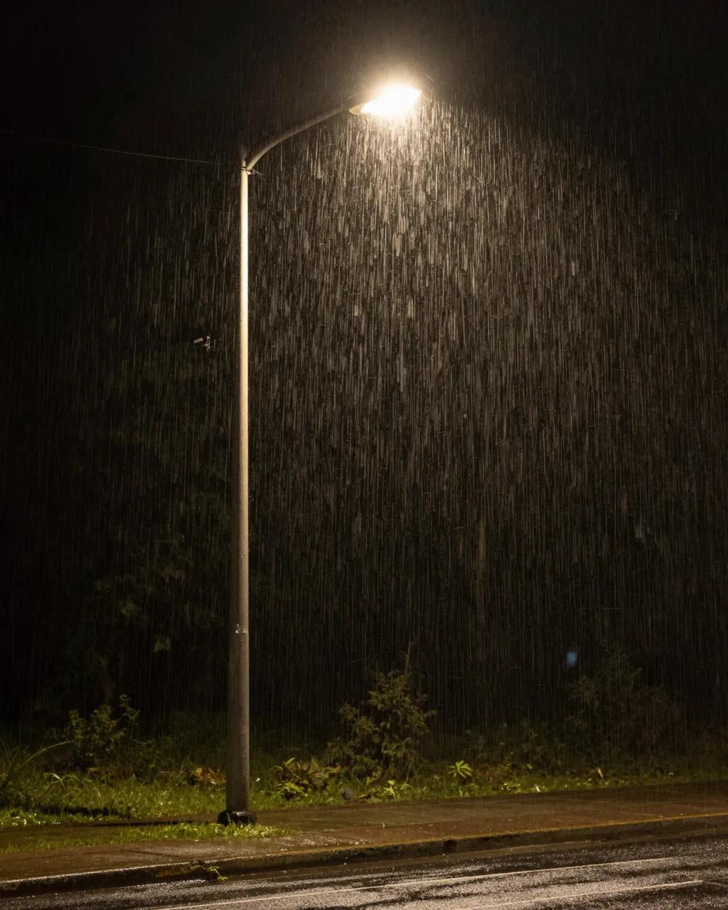 Long exposure view of rain streaking past an illuminated lone street lamp on a wet night roadside