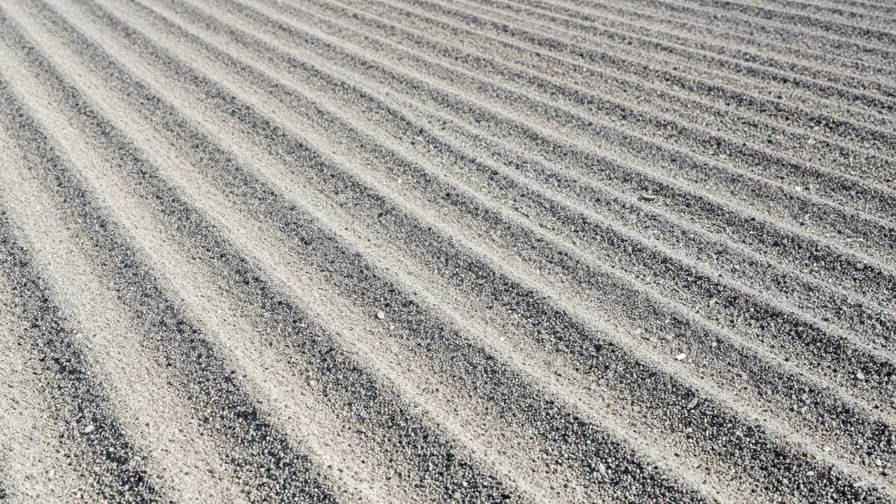 Top view of smooth parallel raked wave patterns across fine gravel under soft light