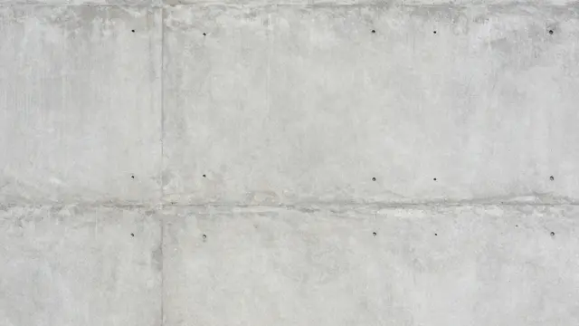 Full frame view of a raw gray concrete wall with formwork seams and evenly spaced tie holes