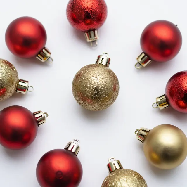 A top-down flat lay of glossy and glittery red and gold Christmas baubles arranged on a plain white background