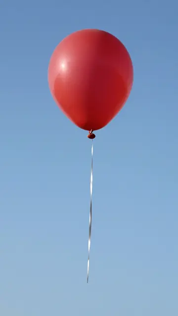 A single glossy red balloon with a thin silver string floats against a clear bright blue sky.