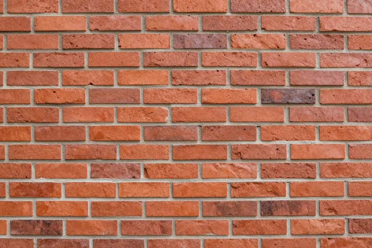 A close up view of a uniform red brick wall with light gray mortar joints