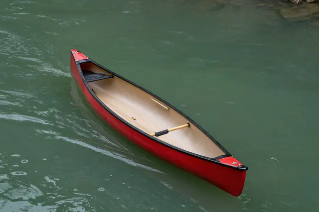 A high-angle view of an empty red canoe floating on calm green river water.
