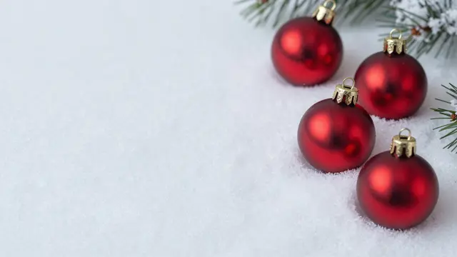 Matte red Christmas baubles rest on fresh snow with empty left copy space and frosted pine sprigs