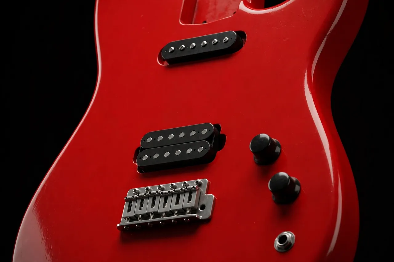 Close-up of a glossy red electric guitar body with pickups against a dark black background