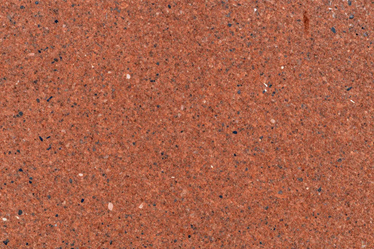 Full frame close-up of a red granite surface scattered with coarse dark and pale mineral crystals