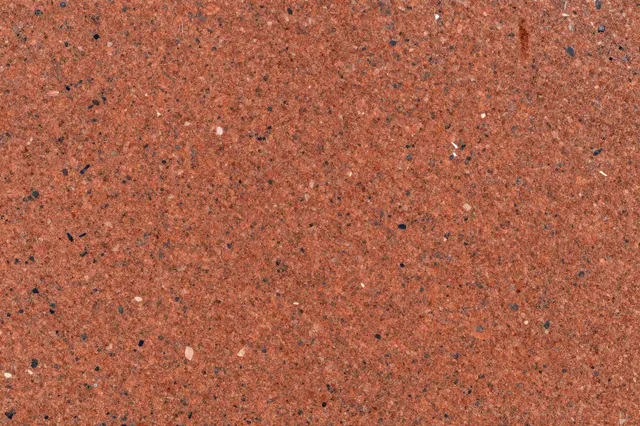Full frame close-up of a red granite surface scattered with coarse dark and pale mineral crystals