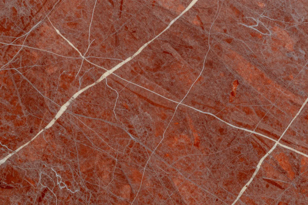 Full frame close-up of polished red marble surface with fine cream and pale gray veins