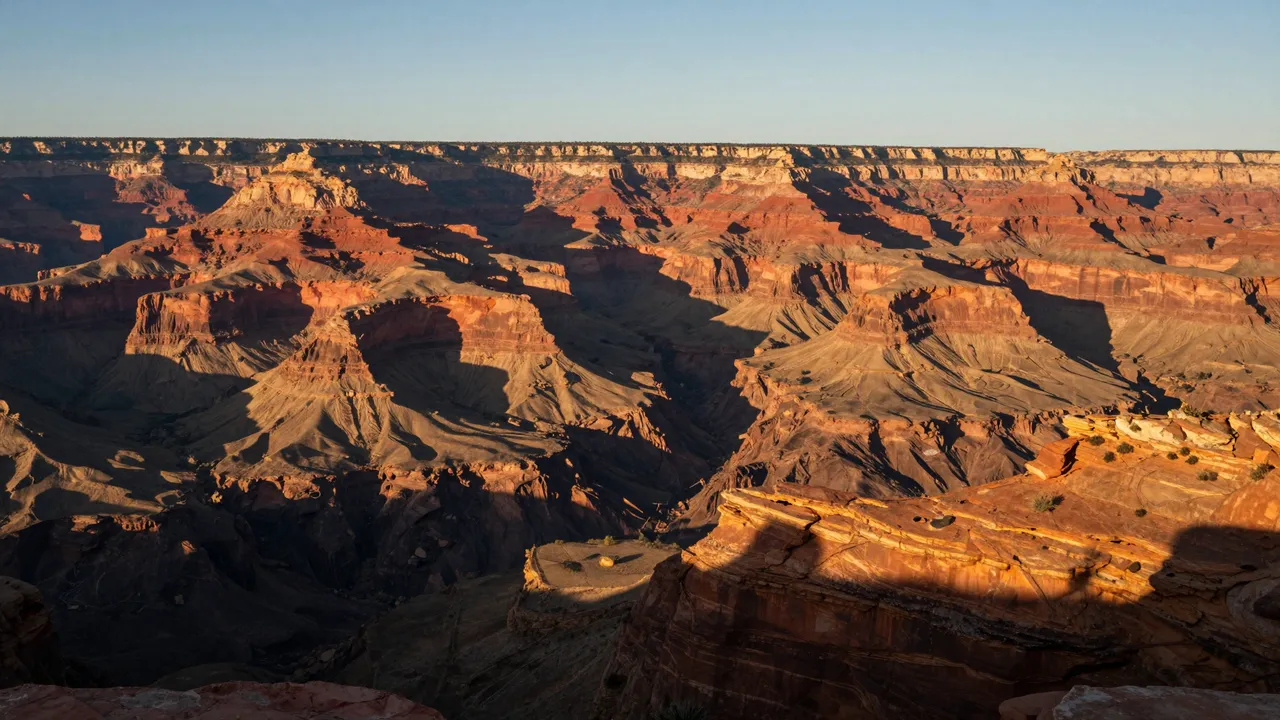 Layered red and orange canyon rock formations are lit by warm low sunset light with dramatic long shadows