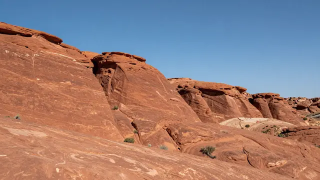 Eroded red sandstone rock formations stretch across the frame under a bright clear blue sky