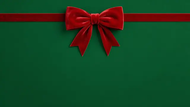 A plush red velvet bow centered on a wide horizontal ribbon over a solid rich green backdrop with empty copy space below.