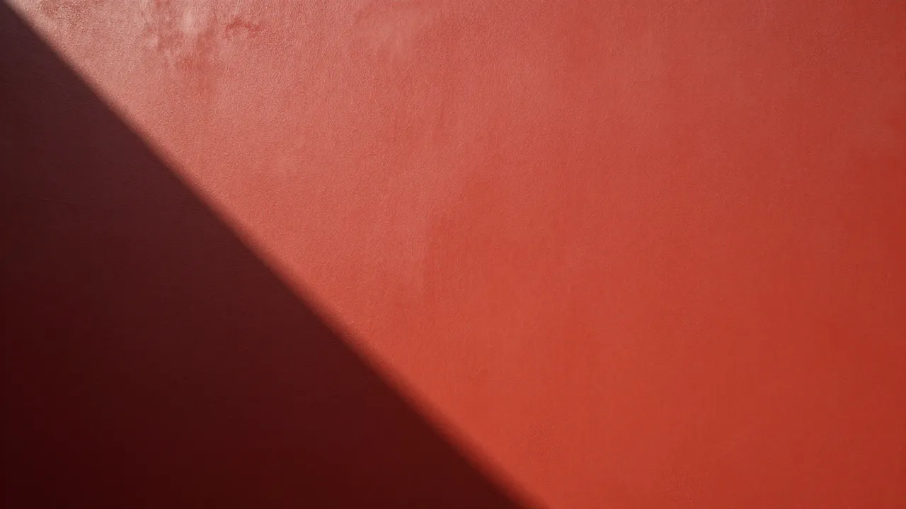 A textured painted red wall with a sharp diagonal afternoon shadow dividing the frame