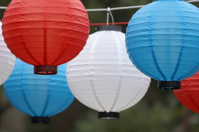 Hanging red, white and blue paper party lanterns arranged in a row against soft blurred green foliage