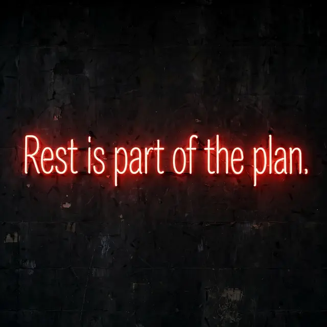 Glowing red neon sign displaying the text "Rest is part of the plan." mounted on a dark textured wall