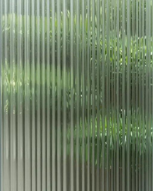 Full frame view of vertical ribbed fluted glass with soft blurred green foliage visible behind it