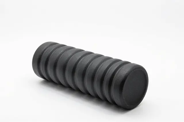 A textured ribbed black foam roller rests diagonally on a plain white studio background.