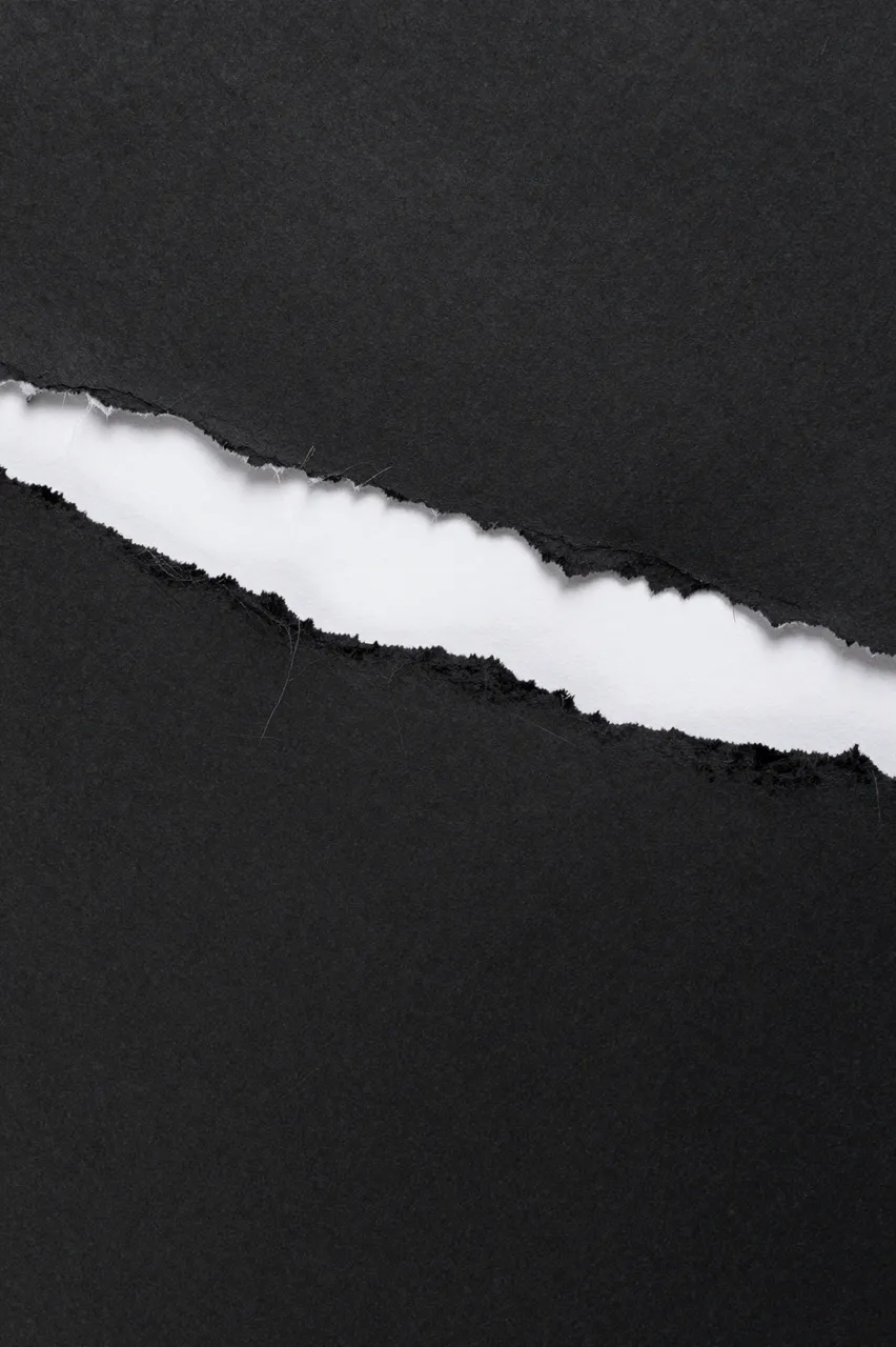 Full frame close up of black paper with a jagged diagonal tear revealing white paper underneath