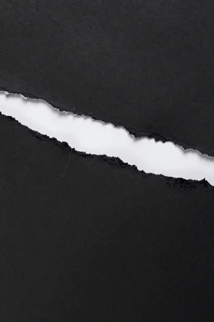 Full frame close up of black paper with a jagged diagonal tear revealing white paper underneath