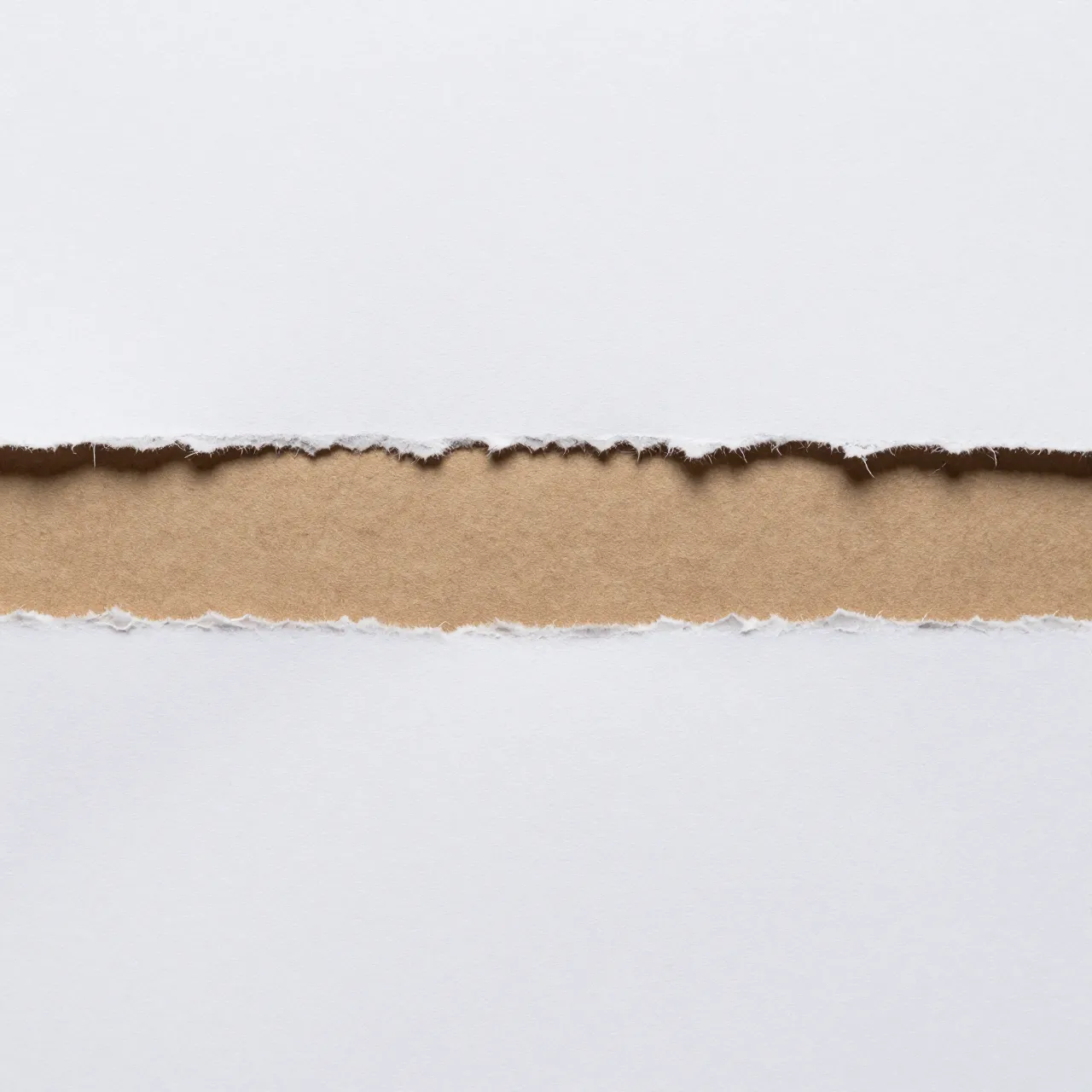Full frame close-up of torn white paper revealing a horizontal strip of brown kraft paper beneath an even, soft light.