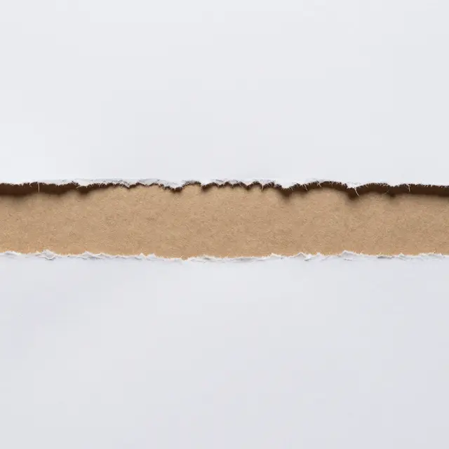 Full frame close-up of torn white paper revealing a horizontal strip of brown kraft paper beneath an even, soft light.