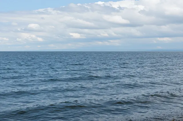 Gentle wind ripples stretch across a blue lake beneath a sky of soft white cumulus clouds