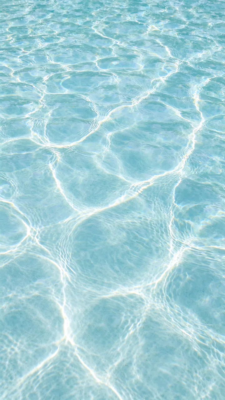 Overhead view of sunlit rippled pale aqua swimming pool water with glowing light refraction lines
