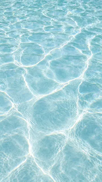Overhead view of sunlit rippled pale aqua swimming pool water with glowing light refraction lines