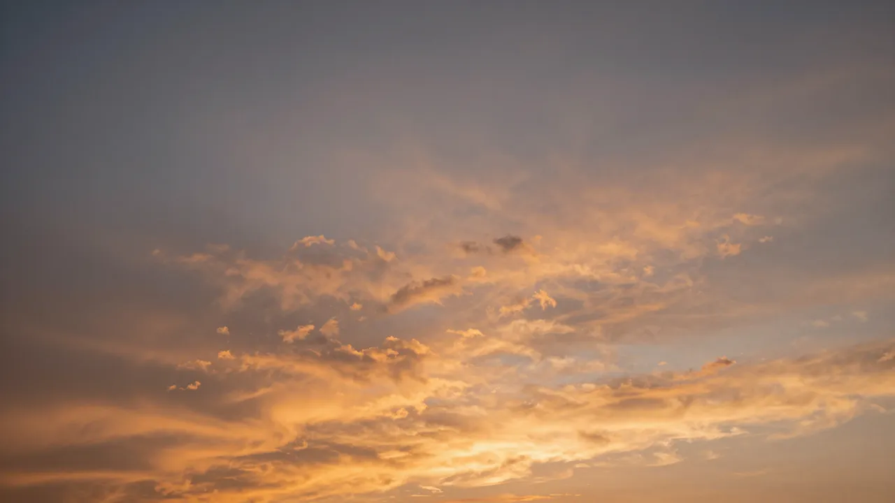 Warm orange-lit rippled altocumulus clouds stretch across a soft dusk sky at sunset