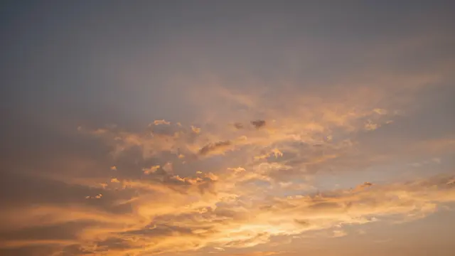 Warm orange-lit rippled altocumulus clouds stretch across a soft dusk sky at sunset