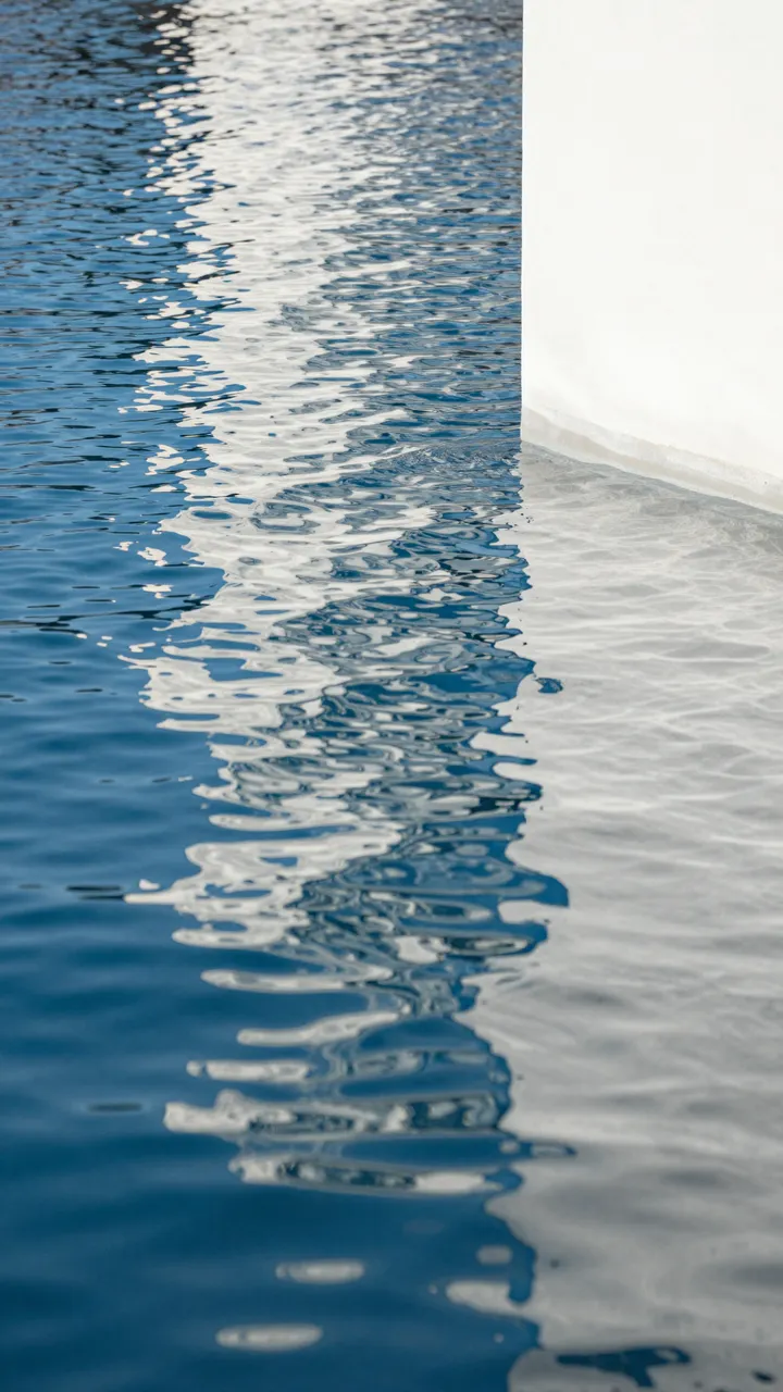 Distorted dancing light reflections of a white vertical surface across rippled deep blue water
