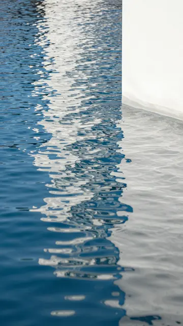 Distorted dancing light reflections of a white vertical surface across rippled deep blue water
