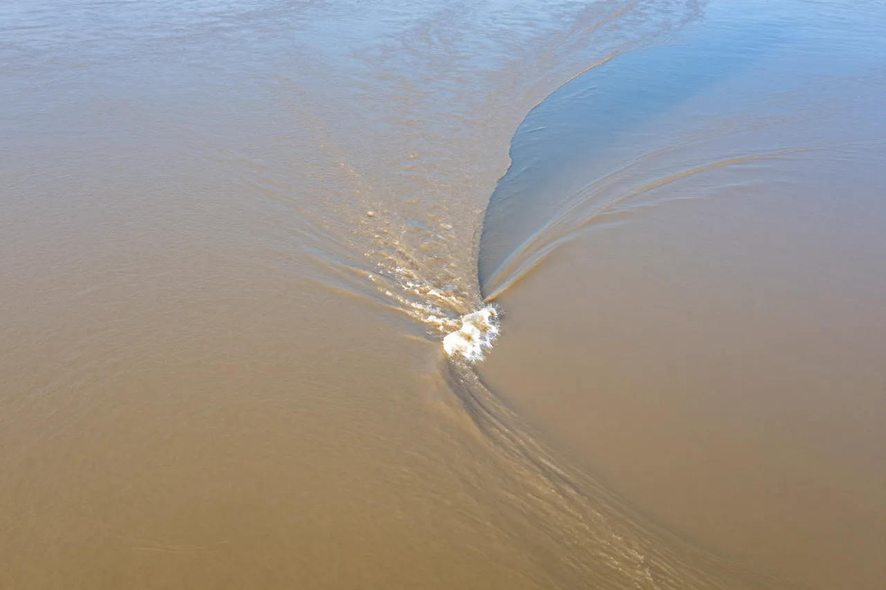 Aerial view of muddy brown and clear blue river water meeting at a sharp confluence with small ripples and foam.
