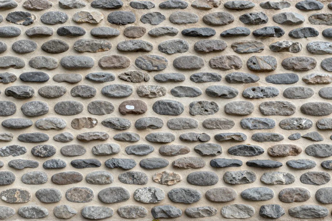 Full frame close-up of a cobblestone wall made of rounded gray and brown river rocks set in pale mortar