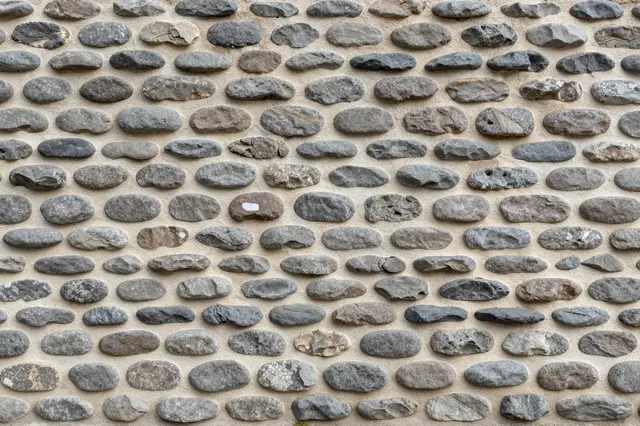 Full frame close-up of a cobblestone wall made of rounded gray and brown river rocks set in pale mortar