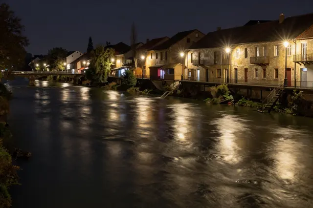 Long exposure view of a flowing river lined with lit historic town buildings at night
