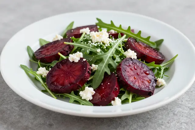 A close-up view of a roasted beet salad with arugula and crumbled goat cheese on a white plate