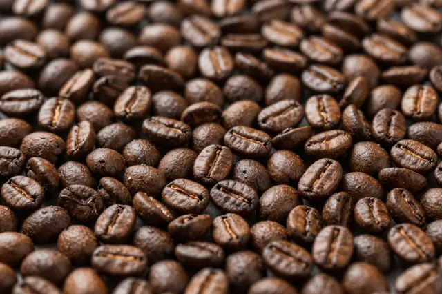 Full frame top view of densely packed roasted coffee beans with soft natural lighting
