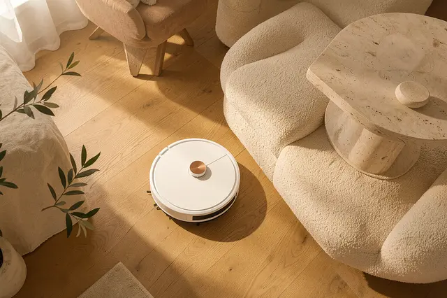 Overhead view of a sleek robot vacuum gliding on oak flooring in a warm sunlit Japandi style living room